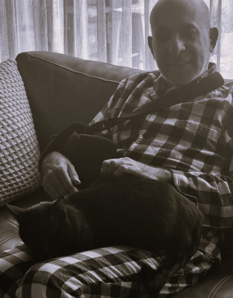 Solly sitting with his arm in a sling and his pet cat on his lap.